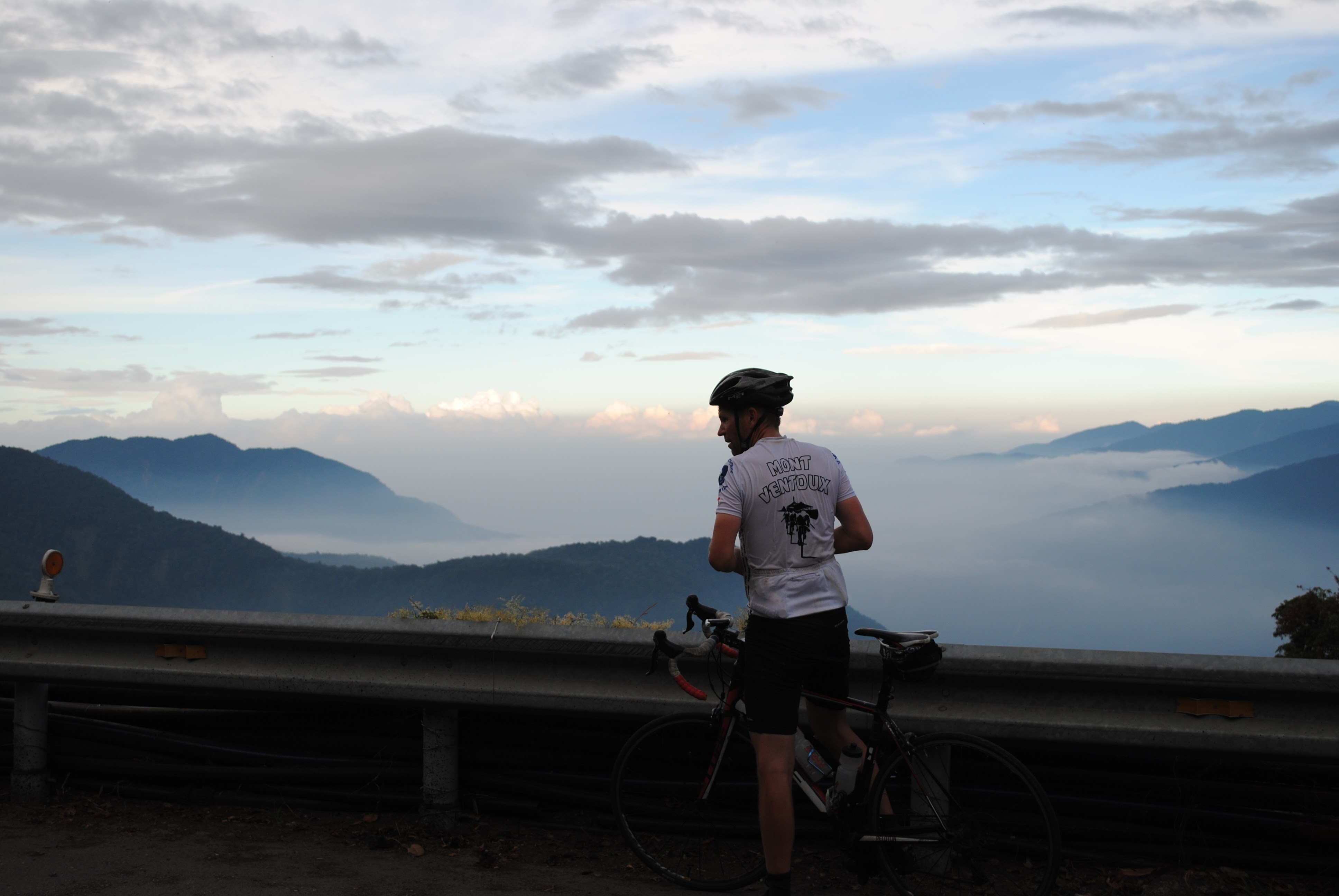 Cyclist pausing at a misty mountain overlook, evocative of the Armenian highlands